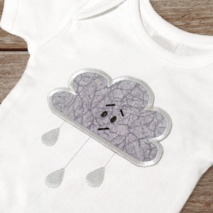 May include: A white baby onesie with a gray embroidered cloud with a face and raindrops hanging from it.