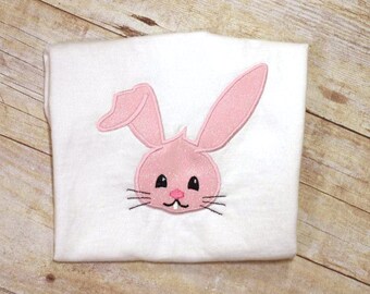 May include: Pink embroidered bunny rabbit face on a white t-shirt.