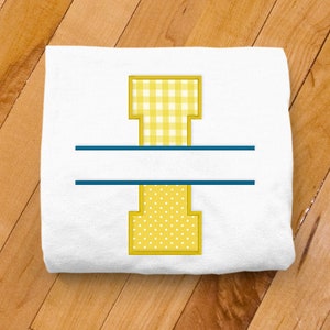 May include: A white t-shirt with a yellow letter I in a split monogram design. The top half of the letter is a yellow and white gingham pattern and the bottom half is a yellow and white polka dot pattern. A blue line separates the two halves of the letter.