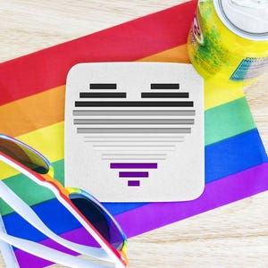 Może przedstawiać: Biały podkładka z czarno-szarym wzorem serca i fioletowym paskiem w środku. Podkładka leży na tęczowej fladze dumy z parą okularów przeciwsłonecznych i puszką napoju.