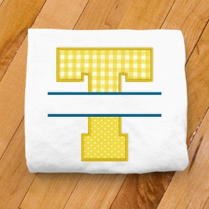May include: A white t-shirt with a yellow letter T. The top part of the T is a gingham pattern and the bottom part is a polka dot pattern. A blue line is centered above the T.