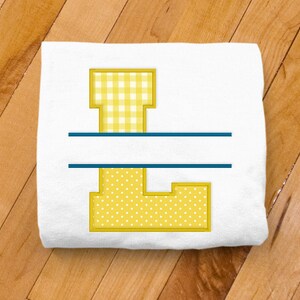 May include: A white t-shirt with a yellow embroidered letter L. The letter is made up of two different patterns, gingham and polka dots. A blue line is centered above and below the letter.