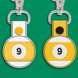 May include: Two leather keychains shaped like a pool ball with the number 9 on them. One keychain has a yellow dot and the other has a black dot.