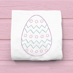 May include: A white fabric with an embroidered Easter egg design. The egg is outlined in purple thread and has a zig-zag pattern in green thread and a row of circles in pink thread.