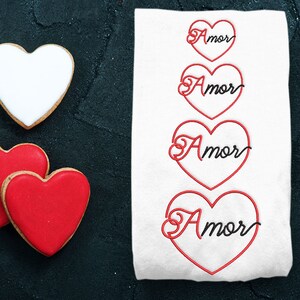 Peut inclure: Quatre broderies en forme de cœur rouge avec le mot "Amor" en écriture cursive noire sur fond blanc.