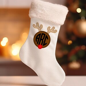 May include: White Christmas stocking with a brown reindeer face and the monogram "ARC" in a circle. The reindeer has a red nose.