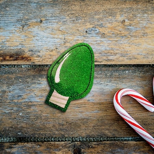 May include: A green glitter Christmas light ornament and two candy canes in the shape of a heart on a rustic wooden background.