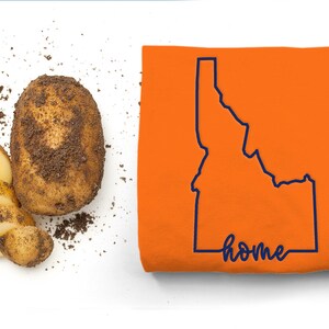 May include: A brown potato with dirt on it, sliced into thin pieces, and a t-shirt with the outline of the state of Idaho and the word "home" written in cursive.