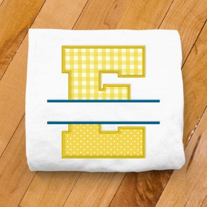 May include: A white t-shirt with a yellow letter E in a split monogram design. The top half of the letter is a gingham pattern and the bottom half is a polka dot pattern. The letter is outlined in gold and the split is outlined in blue.