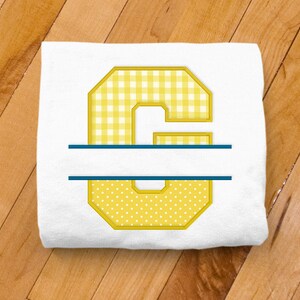 May include: A white t-shirt with a yellow and white gingham letter C with a blue line across the middle. The letter is outlined in yellow.