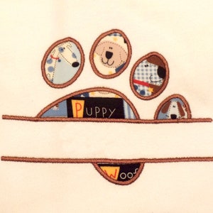 May include: Embroidered paw print design with a brown outline and a white background. The paw print is made up of five circles, each with a different dog face inside. The word "Puppy" is embroidered in black letters inside the paw print. A brown line is embroidered above and below the paw print.