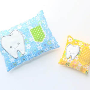 May include: Two tooth-shaped pillows. One is blue with white flowers and a smiling tooth applique. The other is yellow with flowers and a tooth applique. Both have a small pocket.