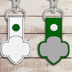 May include: Two keychains with a Girl Scout cookie design. One keychain is white with a green circle and the other is green with a white circle.