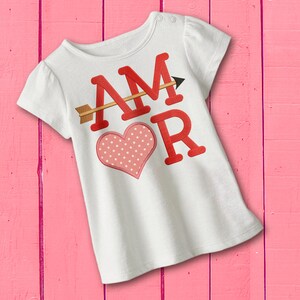 May include: White t-shirt with a red heart and the word "AMOR" in red letters with an arrow through the "M".