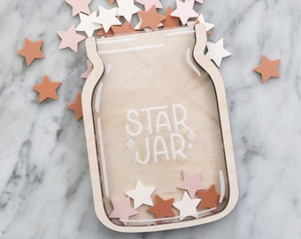Könnte beinhalten: Ein hölzerner Sternentopf mit einer durchsichtigen Vorderseite, gefüllt mit sternförmigen Teilen in Rosa, Weiß und Braun. Der Topf ist mit "STAR JAR" beschriftet.