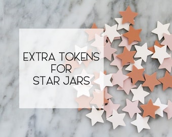 Könnte beinhalten: Zusätzliche Token für Sternengläser. Ein Haufen weißer, rosa und orangefarbener sternförmiger Token auf einer Marmorfläche.