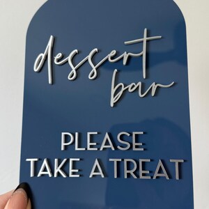 May include: An arched dark blue acrylic sign featuring the text "dessert bar" in a white script font and "PLEASE TAKE A TREAT" in white block lettering. The top of the sign includes the text "EXAMPLE OF METALLIC SILVER ACRYLIC".