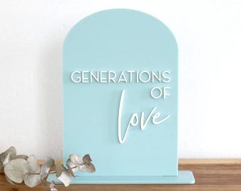 May include: A light blue arched sign with a flat base featuring the white 3D text GENERATIONS OF love. The sign has a smooth, solid-colored surface and is positioned upright. The text is layered on the front, with the word love in script.