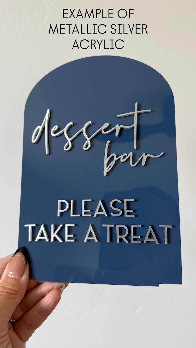 May include: A navy blue acrylic sign with a metallic silver finish. The sign reads "dessert bar" in cursive and "PLEASE TAKE A TREAT" in block letters. The top of the sign is arched.