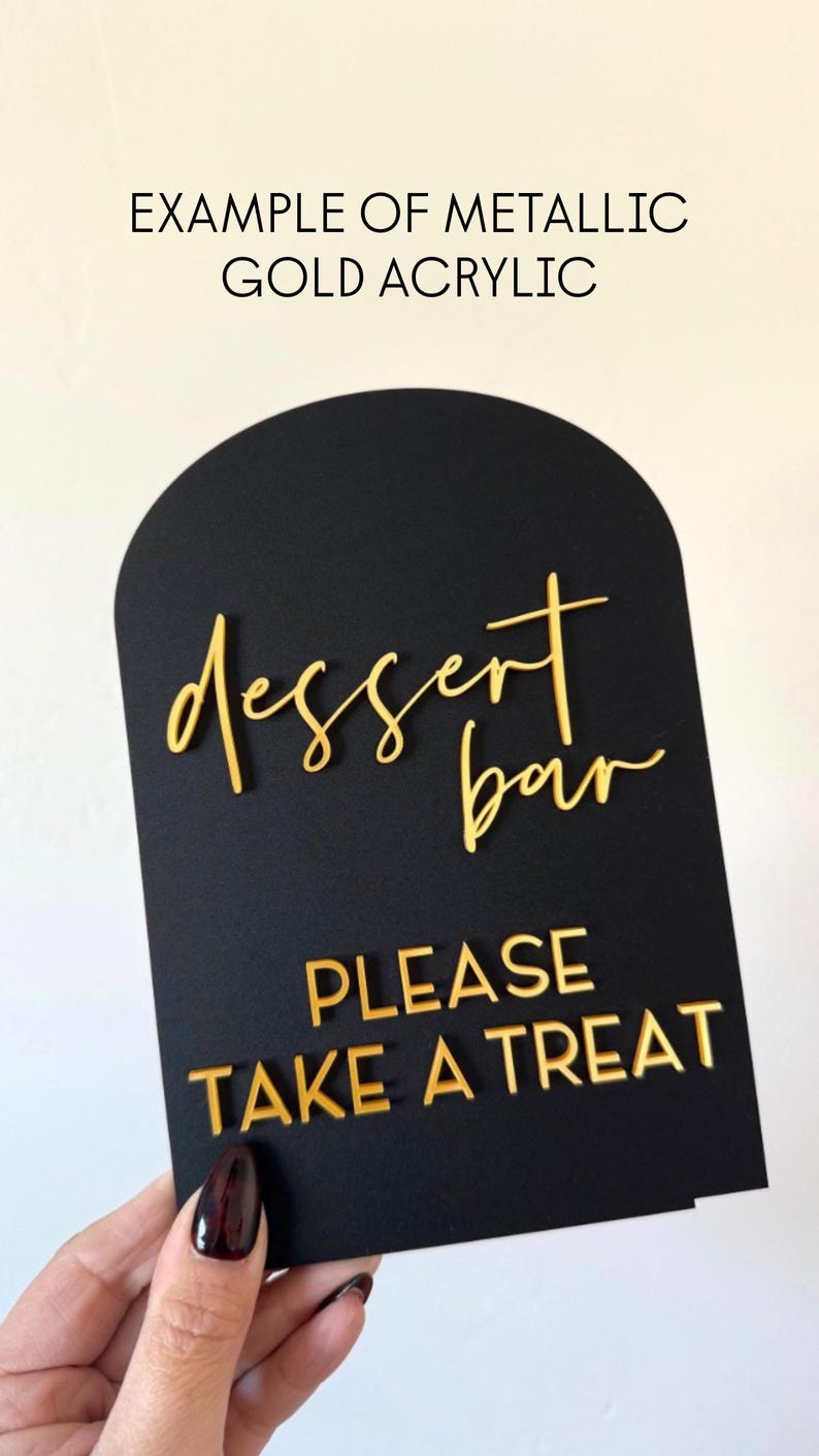 May include: Black acrylic dessert bar sign with gold metallic lettering. The sign reads "dessert bar" in cursive and "PLEASE TAKE A TREAT" in block letters. The top of the sign is arched.
