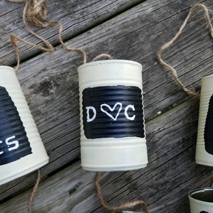 May include: Three white painted tin cans with black painted areas and white lettering. The first can says "Mr & Mrs", the second can says "D&hearts;C", and the third can says "09 01 19".
