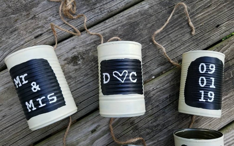 May include: Three white painted tin cans with black painted areas and white lettering. The first can says "Mr & Mrs", the second can says "D&hearts;C", and the third can says "09 01 19".