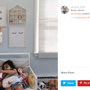 May include: A white toddler bed with a white headboard and footboard. A young girl is sitting on the bed with a variety of stuffed animals. The wall behind the bed is light blue and has three framed prints. One print says "You are my sunshine." Another print has a pair of eyelashes. The third print is a small white house with a window.