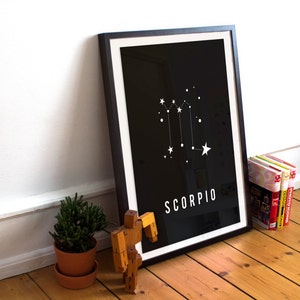 May include: A black framed print with a white constellation design of the Scorpio zodiac sign on a black background. The text "SCORPIO" is printed in white at the bottom of the print.