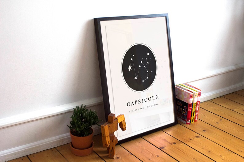 May include: A black framed print with a white background and a black circle containing a constellation of white stars. The text "CAPRICORN" is below the circle, with the words "PATIENT | AMBITIOUS | LOYAL" underneath.