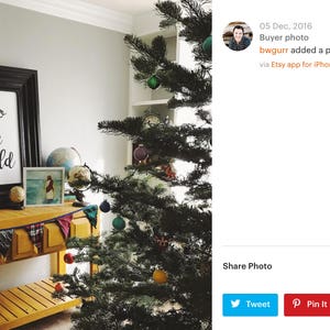 May include: A black framed sign with the text "joy to the world" hanging on a wall above a wooden console table. The table is decorated with a black and white letter board with the text "Let every heart prepare him room", a small wooden figurine, and a garland of colorful fabric scraps. A Christmas tree with green needles and colorful ornaments is in the background.