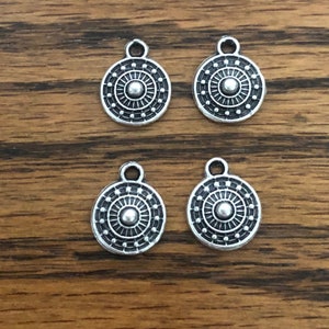May include: Four silver-toned metal charms with a circular design. Each charm features a raised center circle surrounded by concentric circles and dots.