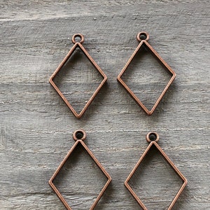 May include: Four copper-colored diamond-shaped metal frames with a loop at the top for hanging. The frames are empty and ready for resin or other embellishments.