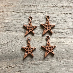 May include: Four copper-colored star-shaped charms with a textured surface. Each charm has a small loop at the top for attaching to a necklace, bracelet, or other jewelry.