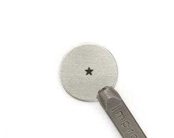 May include: A metal star-shaped punch tool with the text "ImpressArt" on the handle. The punch is being used to create a star-shaped impression on a round metal disc.