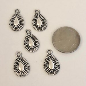 May include: Five silver-colored teardrop charms with a dotted border and a loop at the top. A dime is next to the charms for size comparison. The charms have a simple, elegant design.