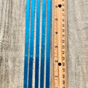May include: Five blue metal strips, each approximately 6 inches long, are lined up next to a ruler. The ruler is marked in inches and shows the length of the strips.