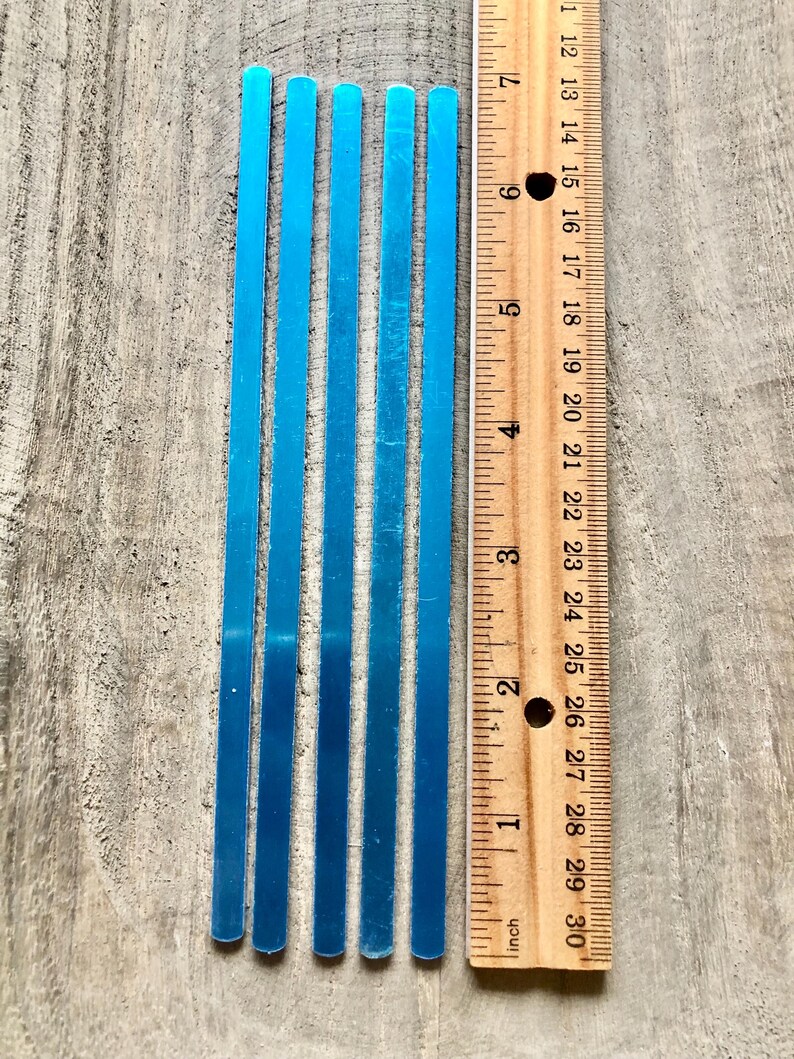 May include: Five blue metal strips, each approximately 6 inches long, are lined up next to a ruler. The ruler is marked in inches and shows the length of the strips.