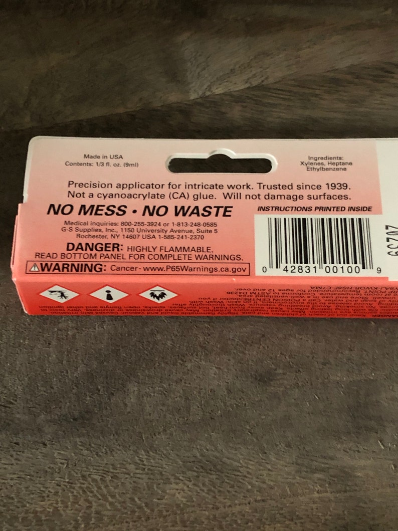 Op de afbeelding: Rood en wit etiket met de tekst "NO MESS NO WASTE" en "DANGER: HIGHLY FLAMMABLE." Het etiket is voor een precisie-applicator voor ingewikkeld werk. Het etiket bevat ook instructies die binnenin zijn gedrukt en een waarschuwing voor kanker.
