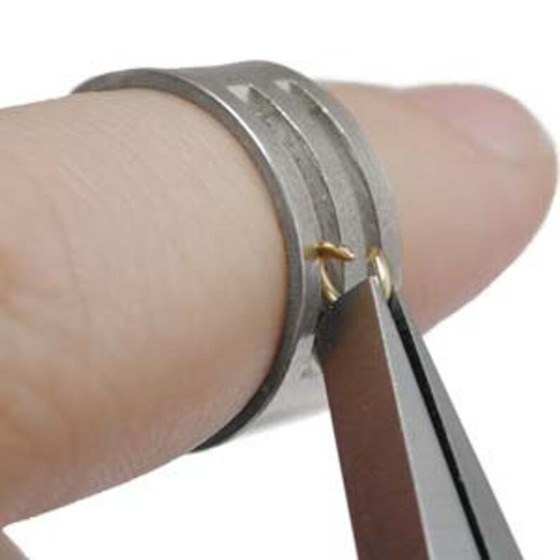 May include: Close-up of a silver ring with a groove on the side. A pair of pliers is holding a small gold loop on the ring.