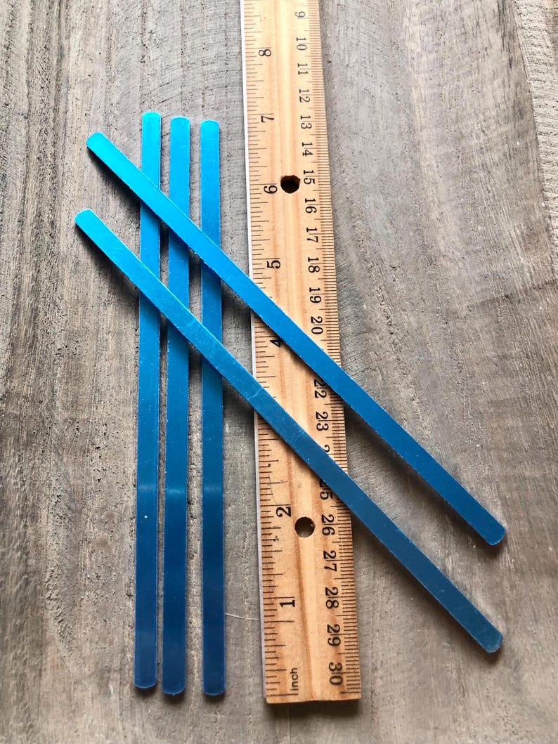 May include: Four blue metal strips, each approximately 9 inches long, are arranged on a wooden surface next to a ruler. The ruler is marked in inches and shows the length of the strips.