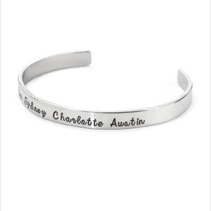 May include: Silver bangle bracelet with the names Sydney, Charlotte, and Austin engraved on it.