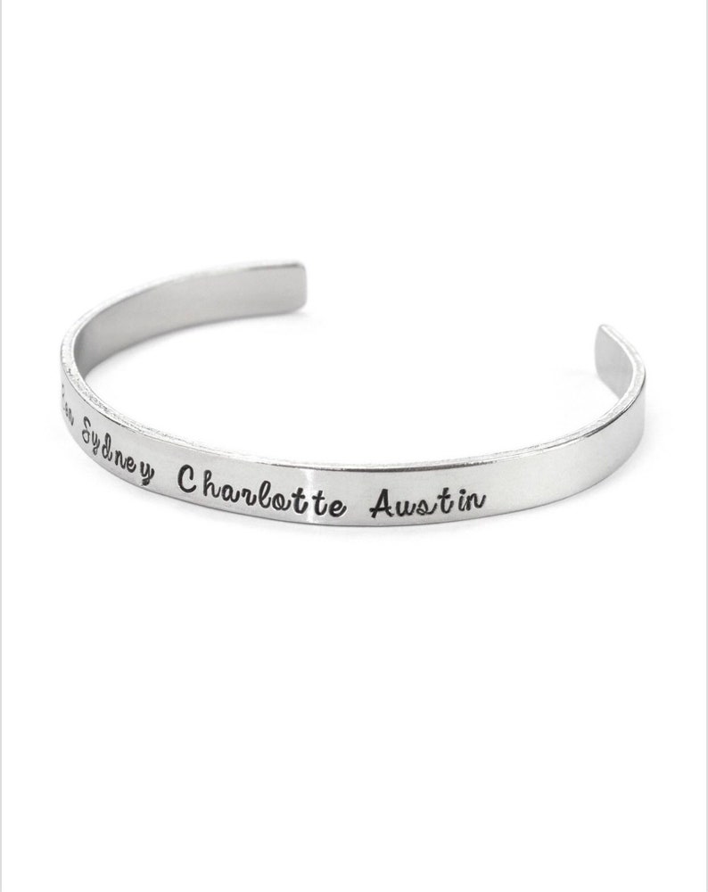 May include: Silver bangle bracelet with the names Sydney, Charlotte, and Austin engraved on it.
