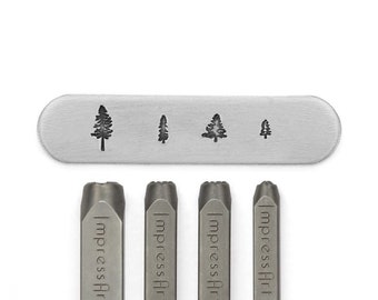 May include: A set of metal stamping tools with tree designs. The set includes four stamps with different tree silhouettes and four metal stamps with the text "ImpressArt". The tools are silver-colored and are on a white background.