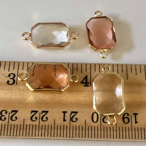 May include: Four gold-toned connector charms with faceted glass inserts. Two charms have clear glass inserts and two charms have light brown glass inserts. The charms are shown next to a ruler, measuring approximately 1 inch in length.