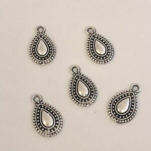 May include: Five silver-colored teardrop charms with a textured border of small dots. Each charm has a loop at the top for attaching to jewelry. The teardrop shape has a smooth, reflective center.