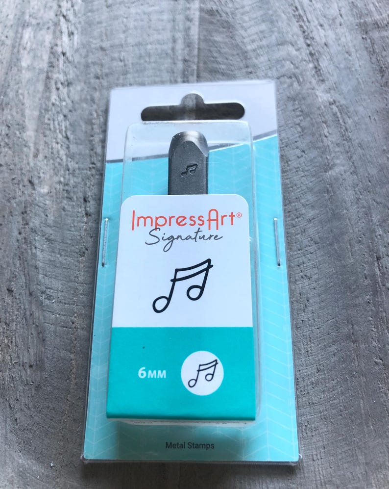 May include: A silver metal stamp with a music note design. The stamp is packaged in a clear plastic blister pack with a blue and white background. The packaging includes the brand name "ImpressArt Signature" and the size of the stamp, "6mm".