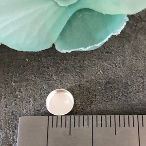 May include: A silver-colored, round, flat-backed cabochon with a white center, measuring approximately 1 cm in diameter.