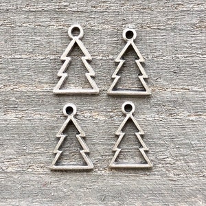 May include: Four silver metal Christmas tree charms with a loop at the top. The charms are on a gray wooden background.