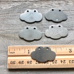 May include: Five metal cloud-shaped charms with two holes each. The charms are approximately 1 inch in size and are shown next to a ruler.