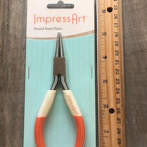May include: A pair of orange and white round nose pliers packaged on a white card with the text "Impress Art" and "Round Nose Pliers".